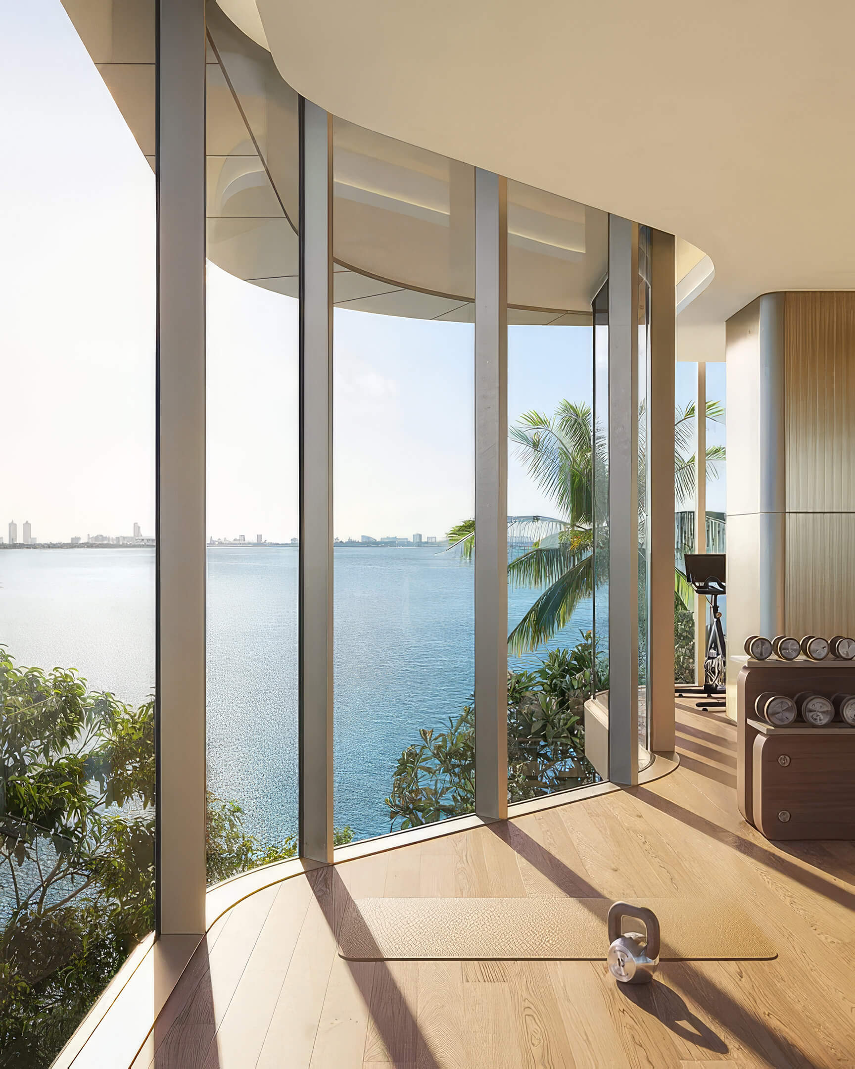 Fitness area at Lilli Miami Edgewater with dumbbells beside curved windows overlooking the bay